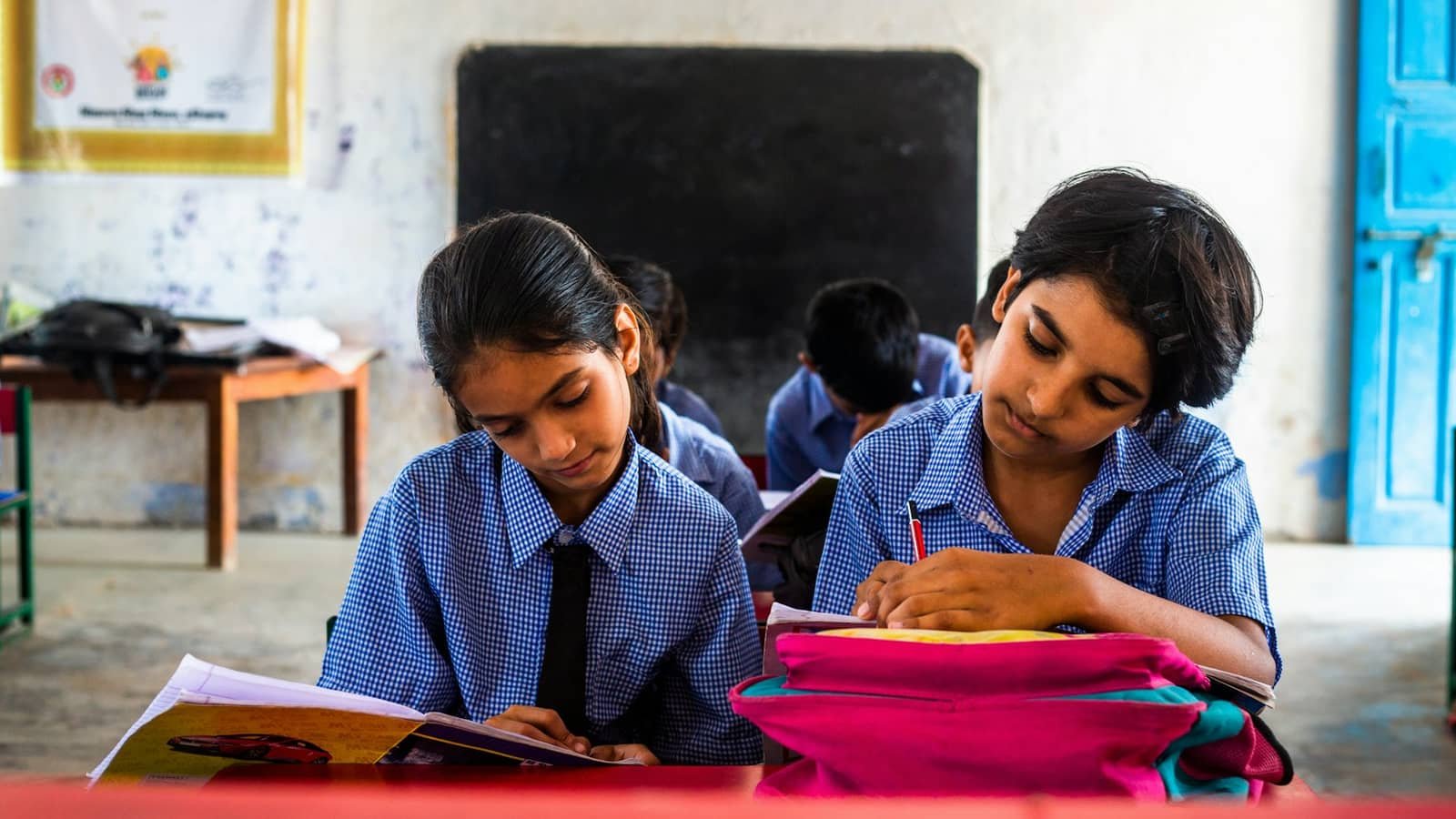 Two schoolgirls in uniform writing in notebooks at a classroom desk